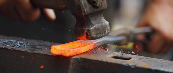 Detail shot of hammer forging hot iron at anvil